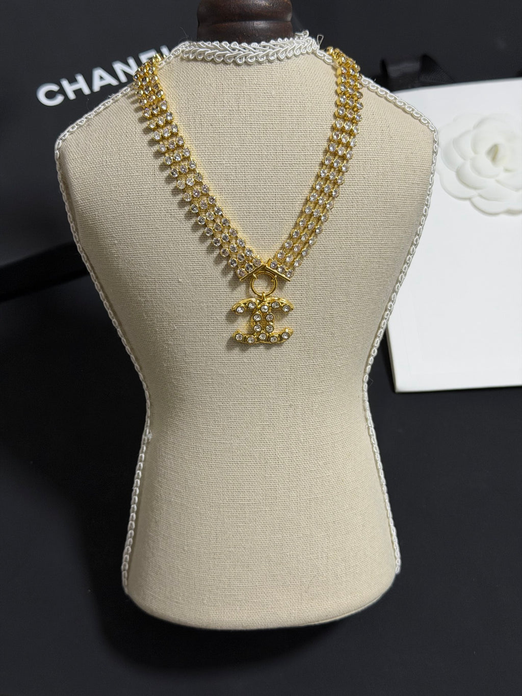 Gold-tone rhinestone necklace with CC bow pendant on beige display bust