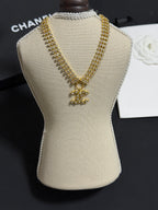 Gold-tone rhinestone necklace with CC bow pendant on beige display bust
