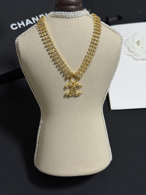 Gold-tone rhinestone necklace with CC bow pendant on beige display bust
