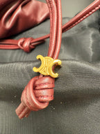 Gold-tone clasp on burgundy braided leather cord with knotted end