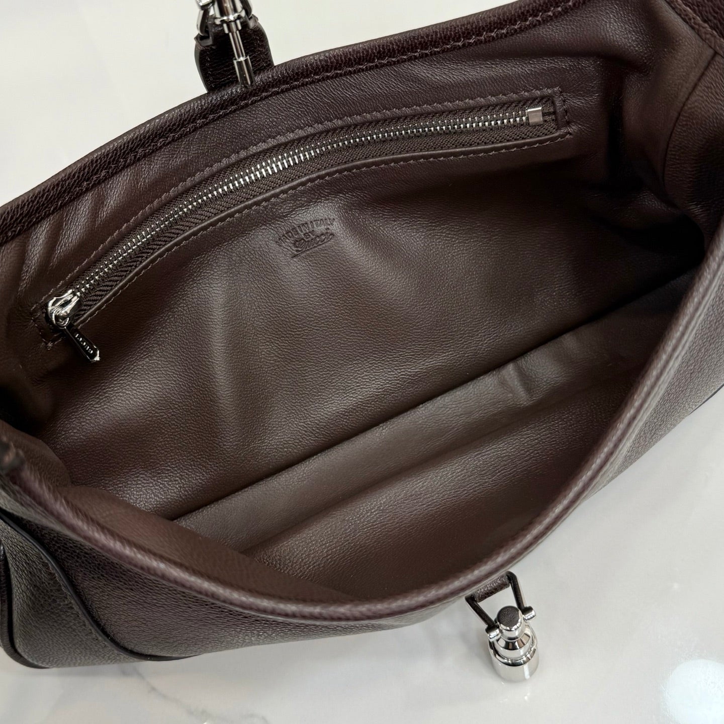 Dark leather hobo bag interior with zippered pocket and metal snap tab at base