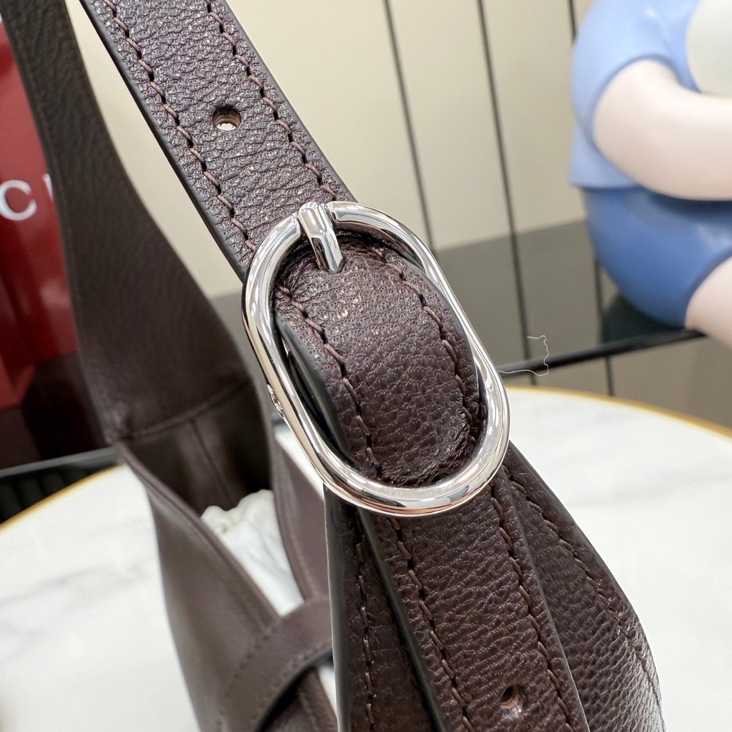 Dark leather hobo bag strap detail with metal O-ring and stitched connection point