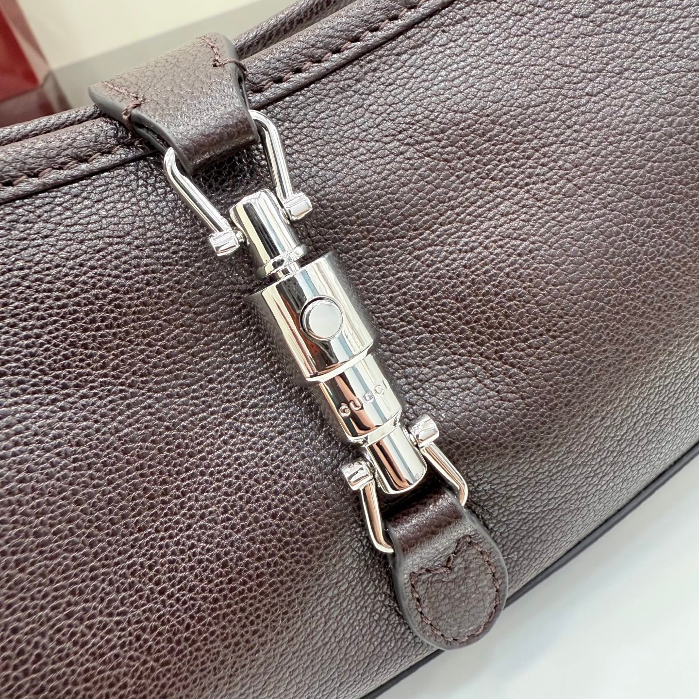 Dark leather hobo bag clasp close-up with silver-tone hardware and stitched edge