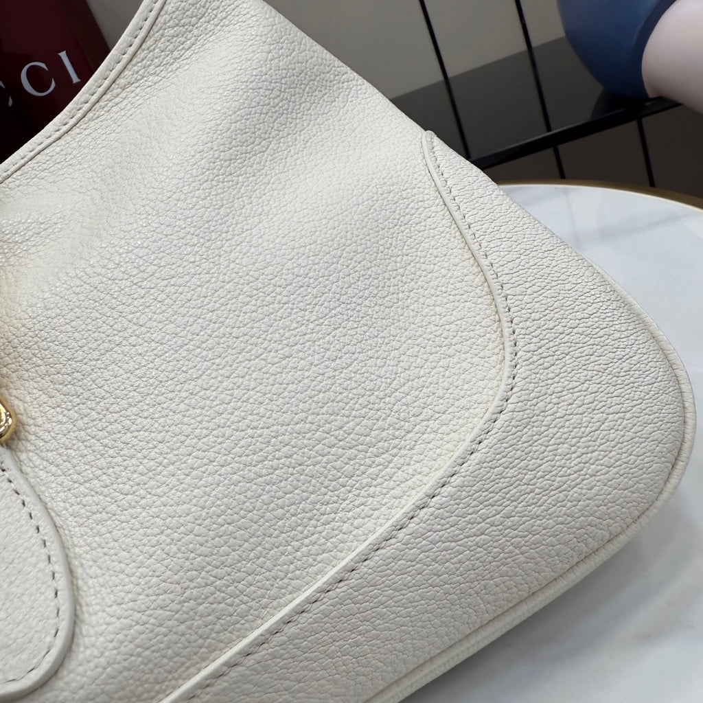 White textured leather bag side with curved seam and partial gold hardware
