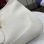 White textured leather bag side with curved seam and partial gold hardware