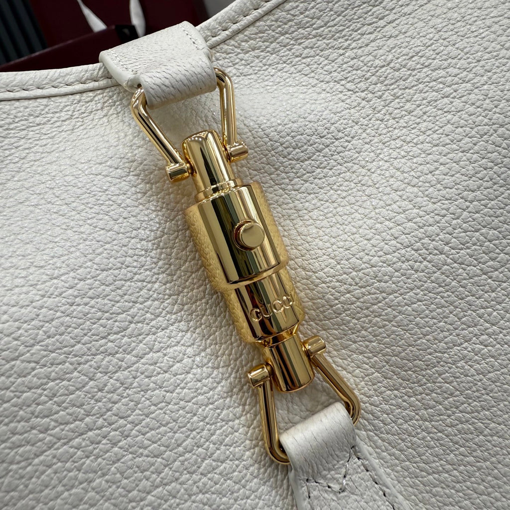 Gold-tone bag lock clasp on textured white leather strap