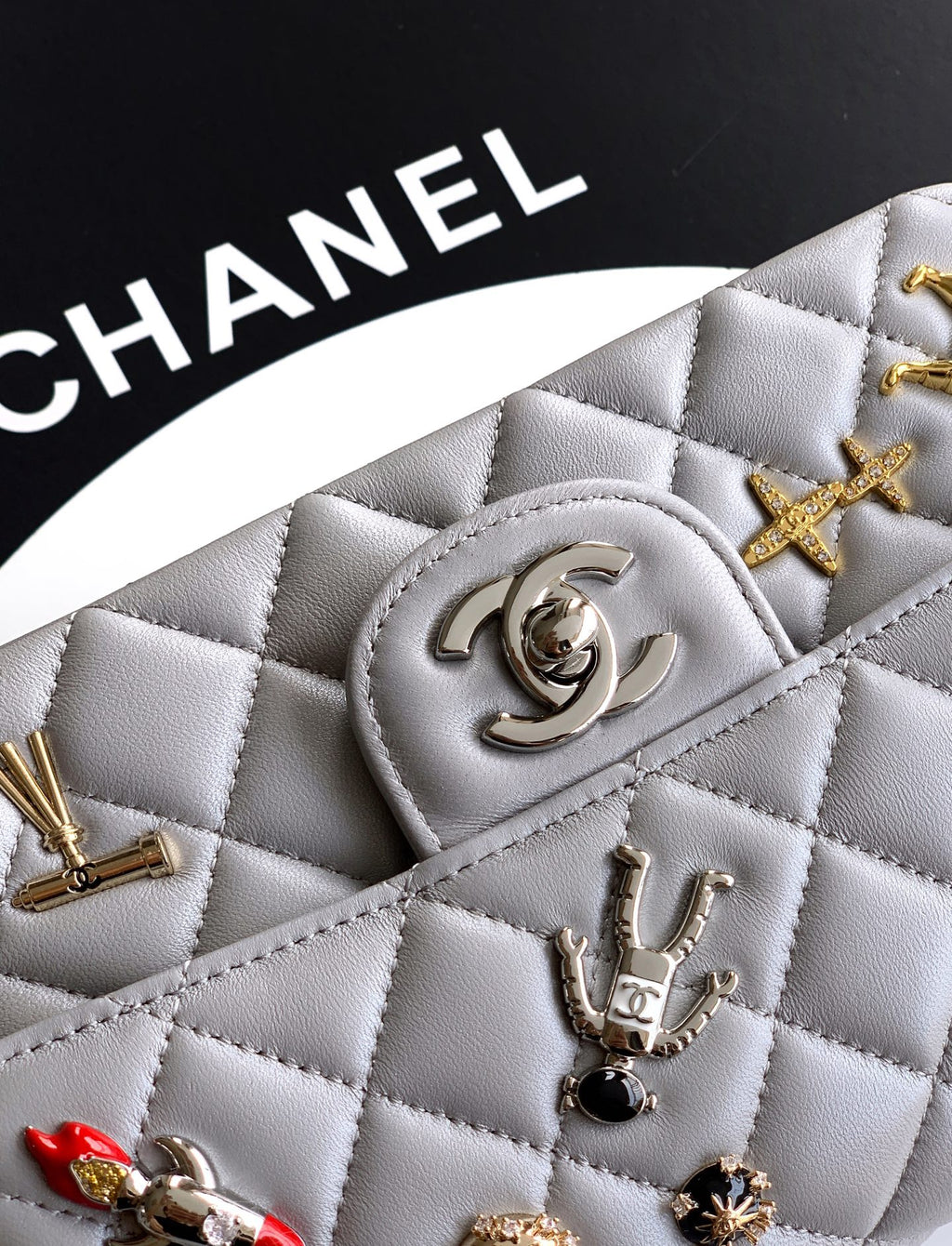 Close-up quilted leather flap with Chanel logo and gold-tone charms, gray