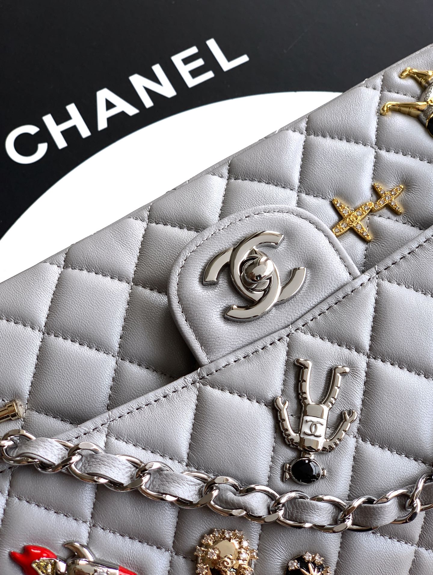 Chanel quilted light gray bag close-up with CC medallion, stud charms, and chain