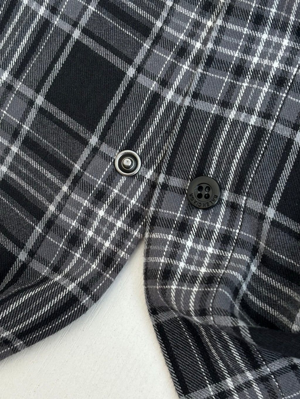 Close-up of plaid long-sleeve shirt with dark buttons and metal snap near hem