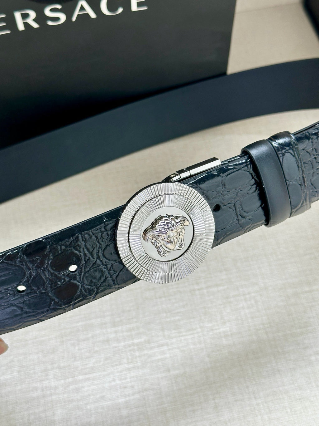 Dark blue embossed leather belt with round silver Medusa buckle, close-up