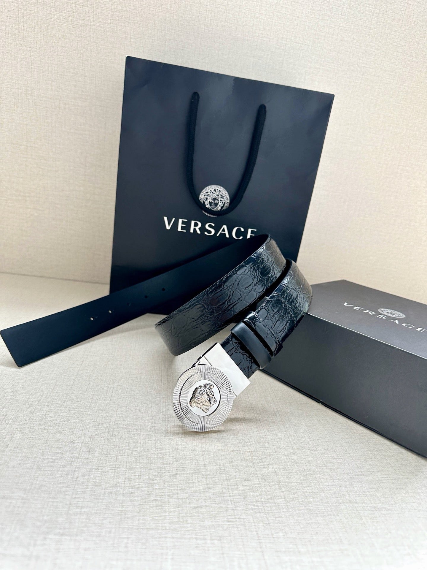 Dark blue leather belt with round silver Medusa buckle, resting on boxes