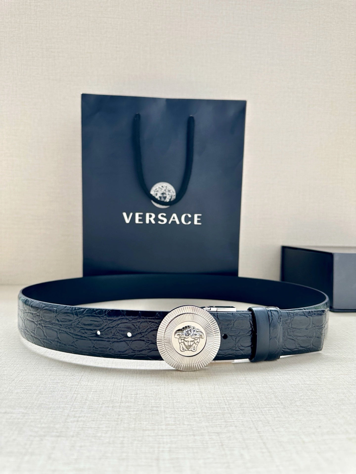 Dark blue leather belt with embossed texture and round silver Medusa buckle