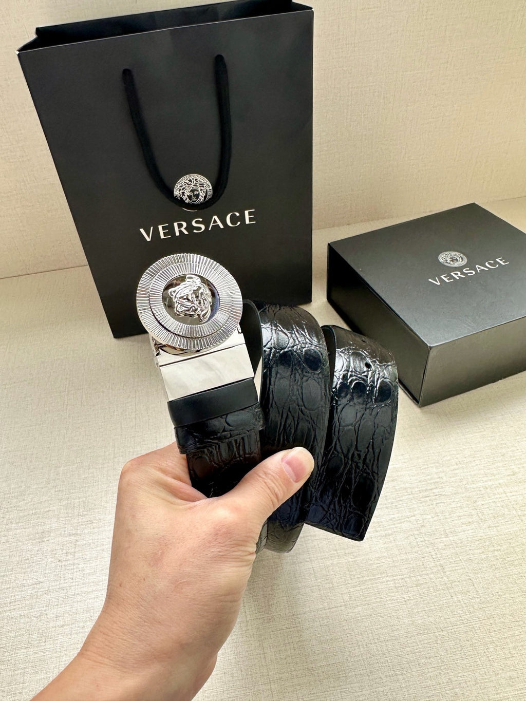Dark blue embossed leather belt held in hand, showing round silver Medusa buckle