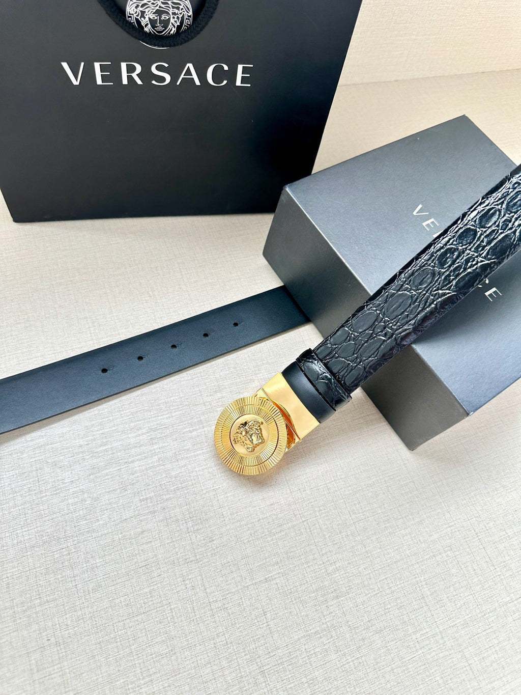Dark leather belt with gold Medusa round buckle and visible adjustment holes