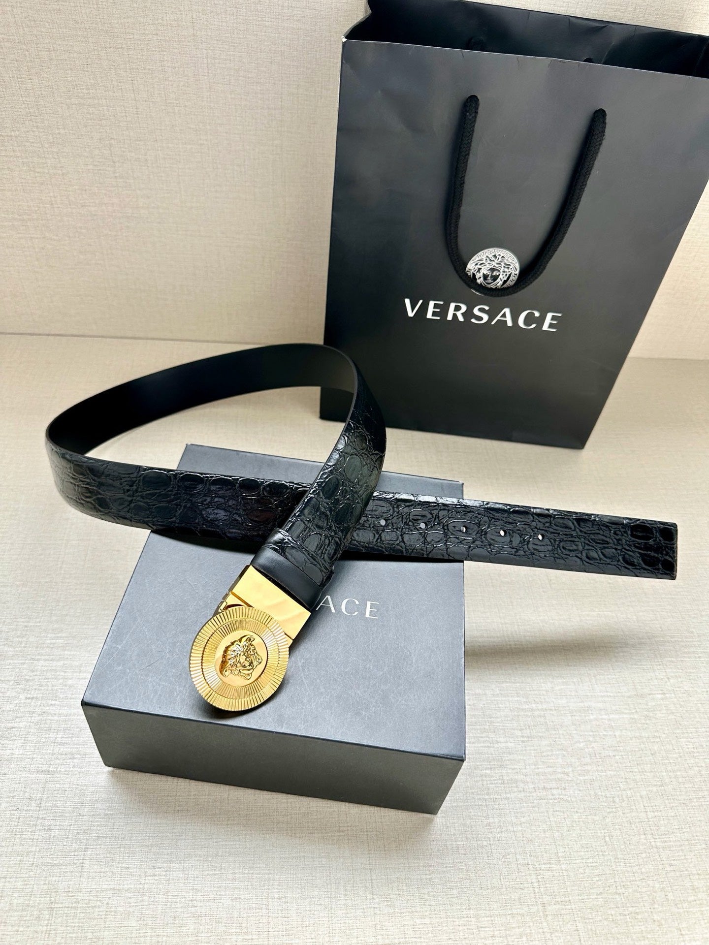 Dark embossed leather belt with gold Medusa round buckle and extended strap