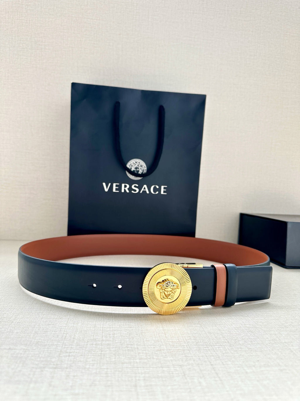 Versace belt with gold medallion buckle and dark navy strap, orange underside accent
