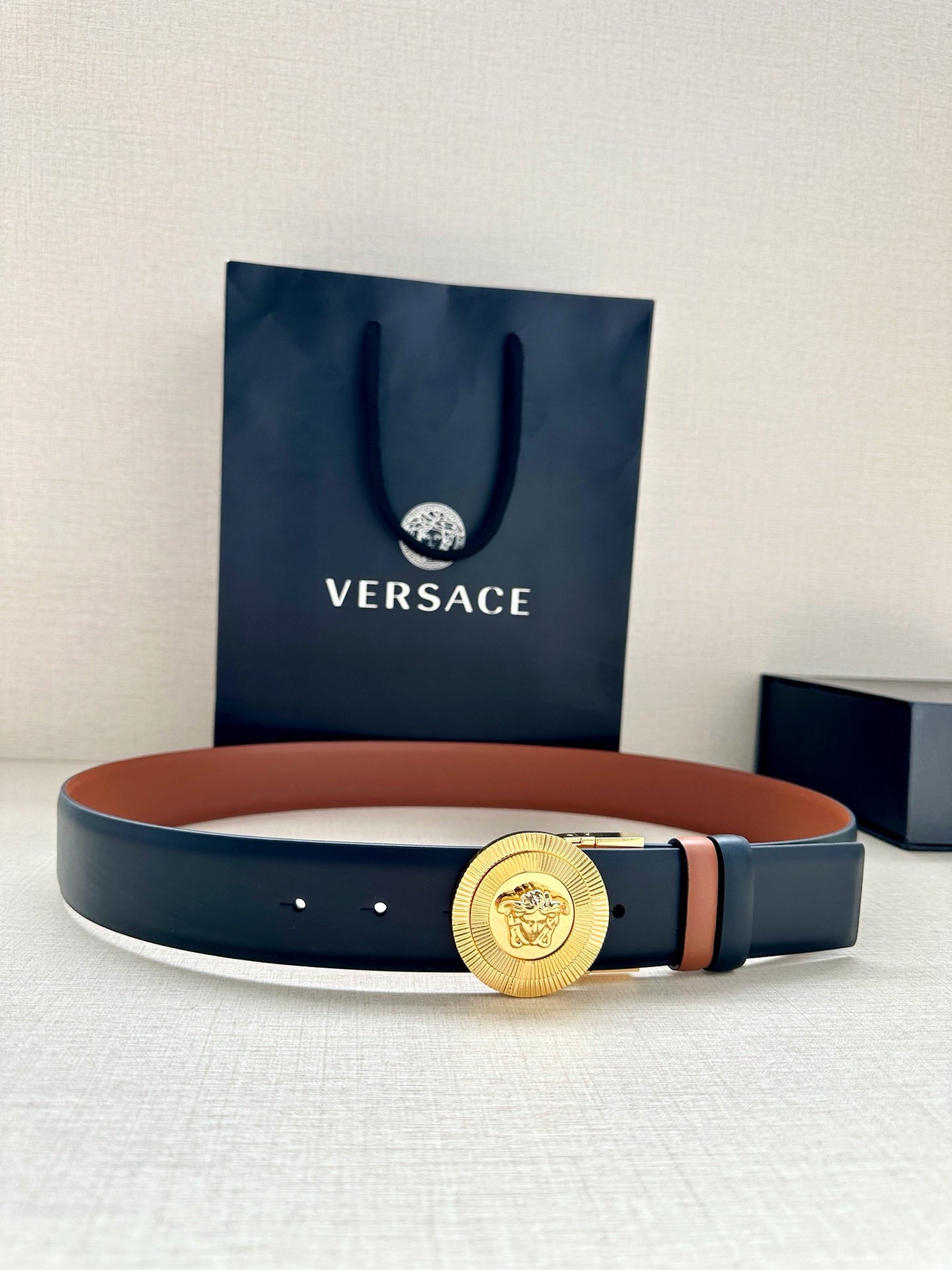 Versace belt with gold medallion buckle and dark navy strap, orange underside accent