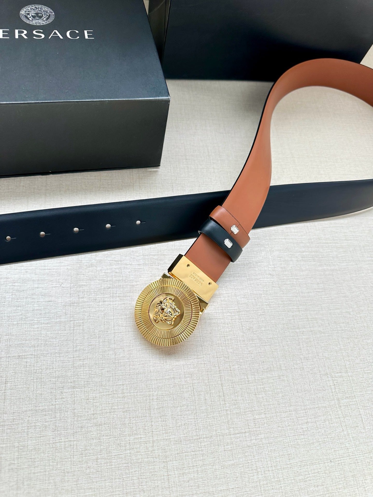 Versace belt detail: gold medallion buckle on dark navy leather, orange edge trim