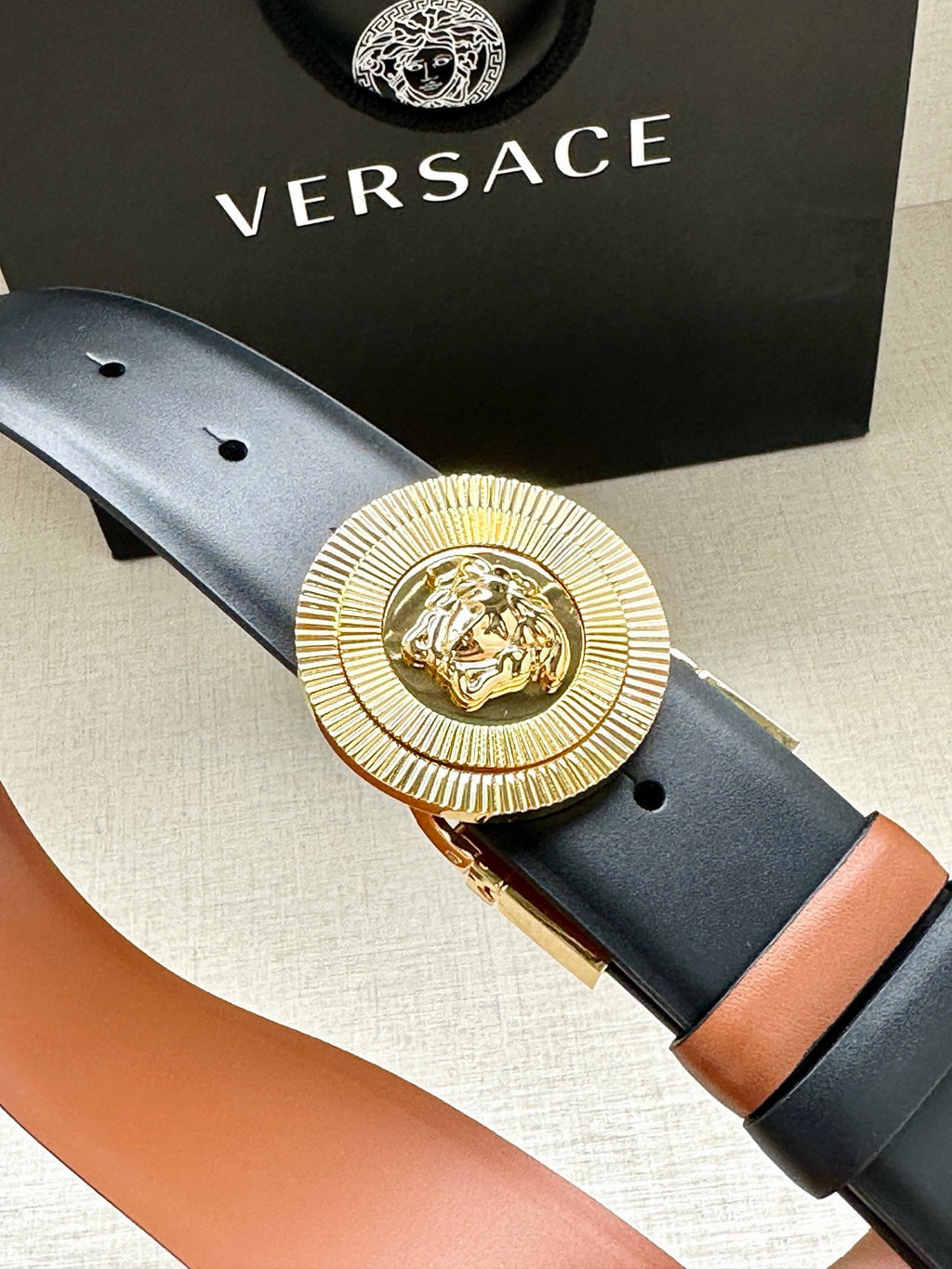 Versace belt close-up: gold medallion buckle on dark navy leather with orange lining