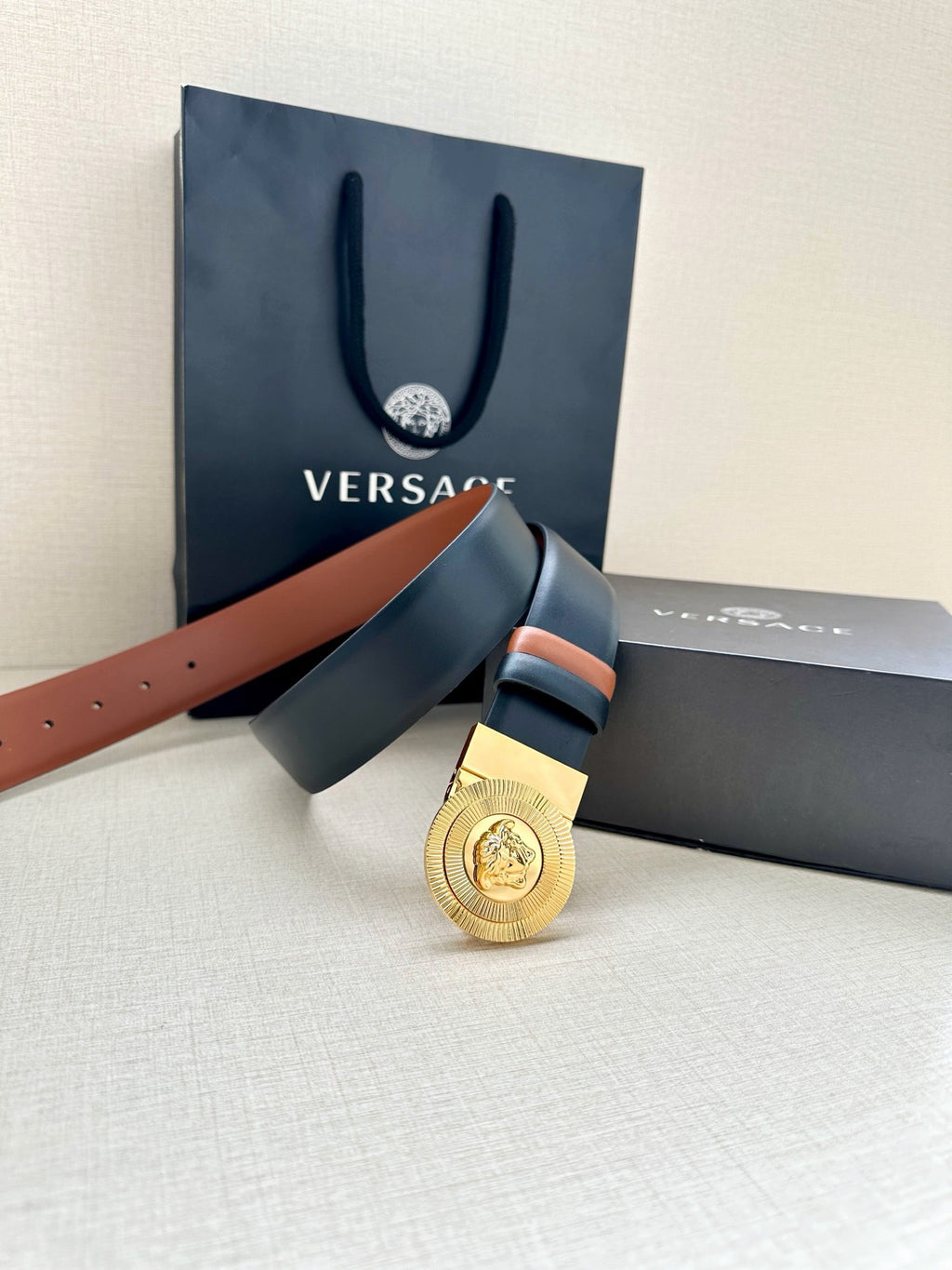 Versace belt featuring gold round medallion buckle on dark navy strap with orange edges