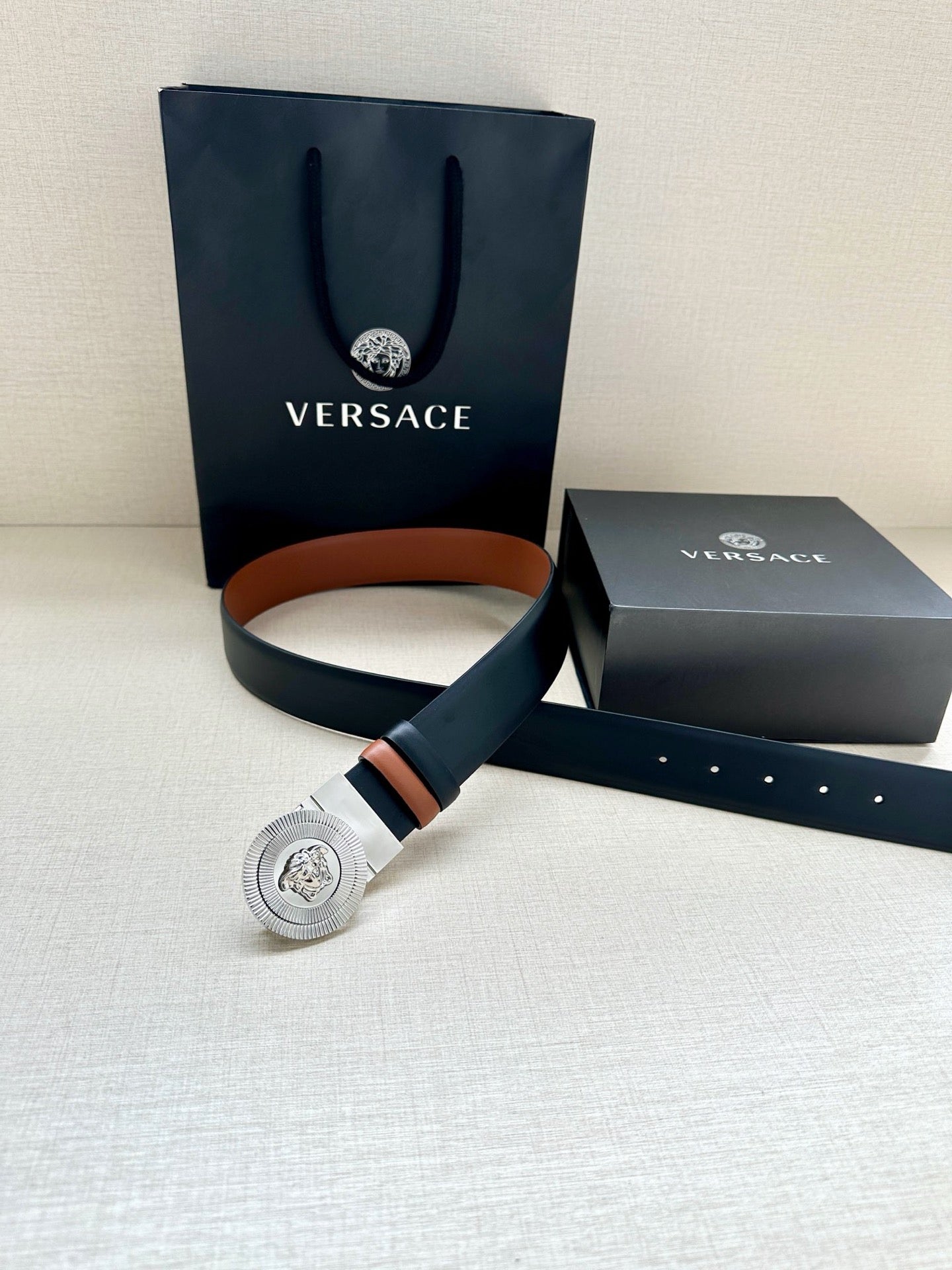 Dark navy leather belt with silver Medusa buckle and tan strap underside lining
