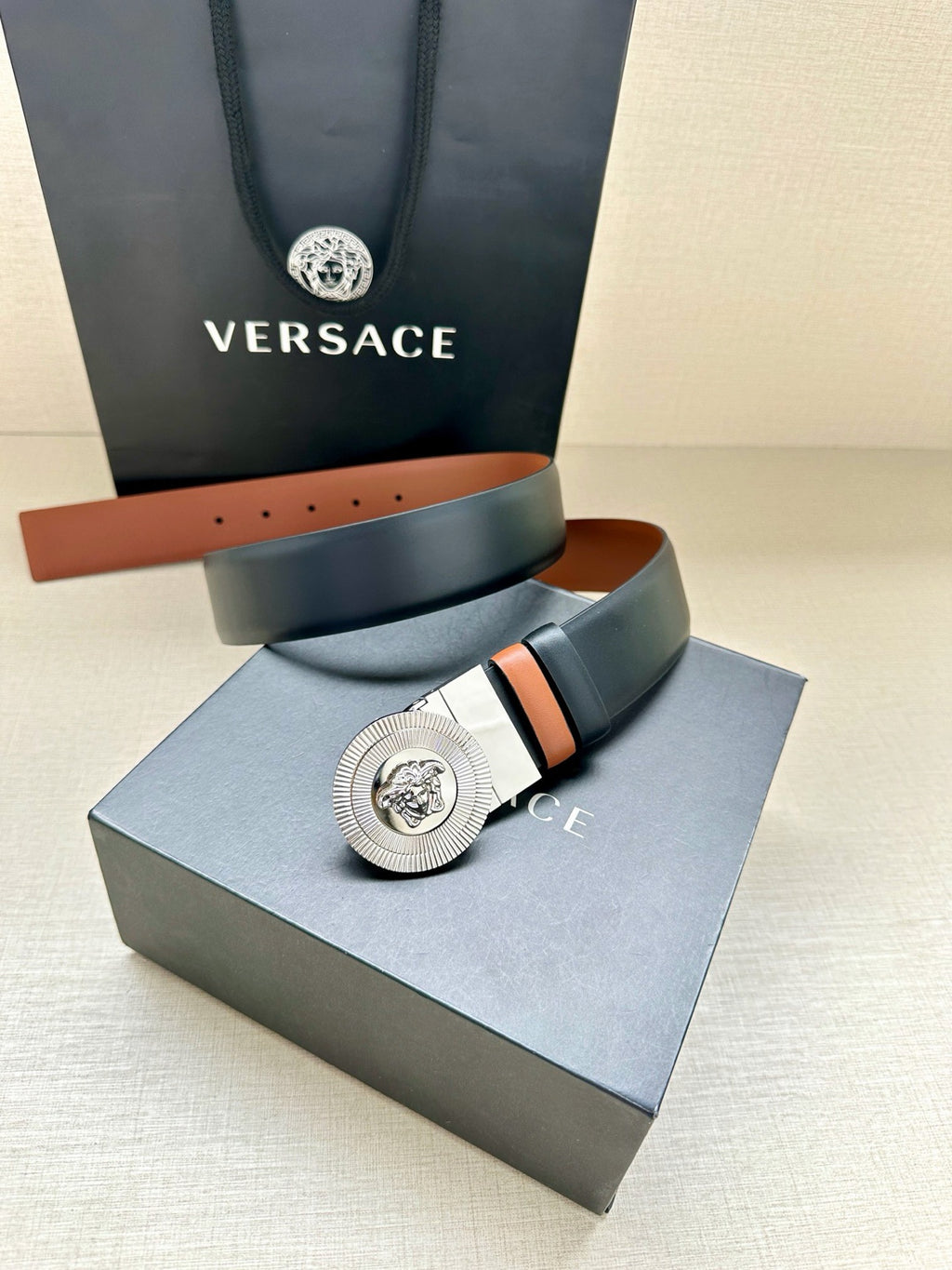 Navy leather belt with round silver Medusa buckle on a tan-lined strap