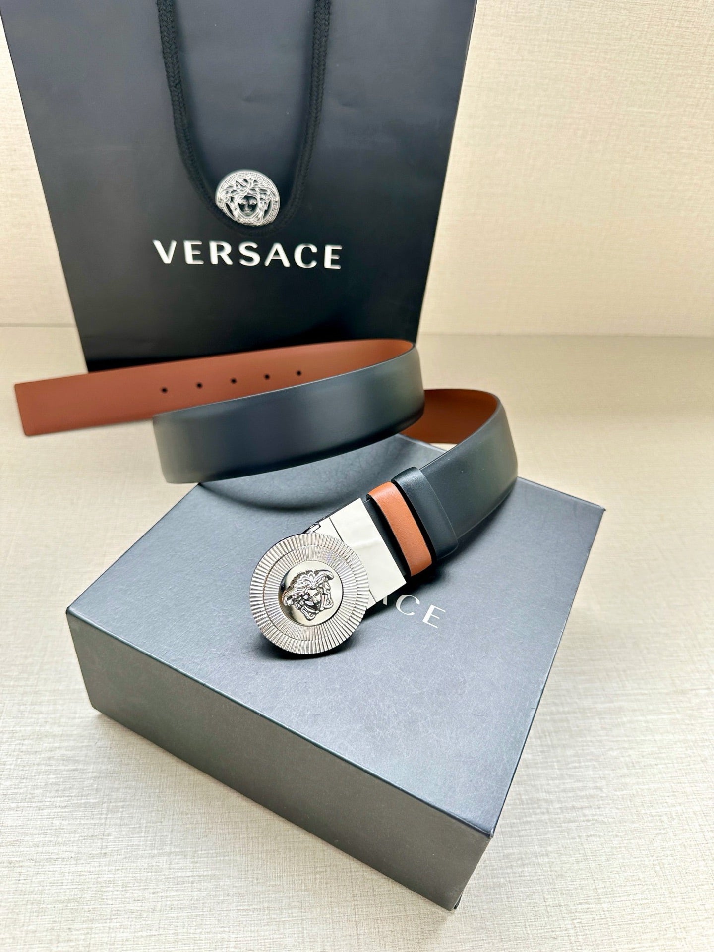 Navy leather belt with round silver Medusa buckle on a tan-lined strap