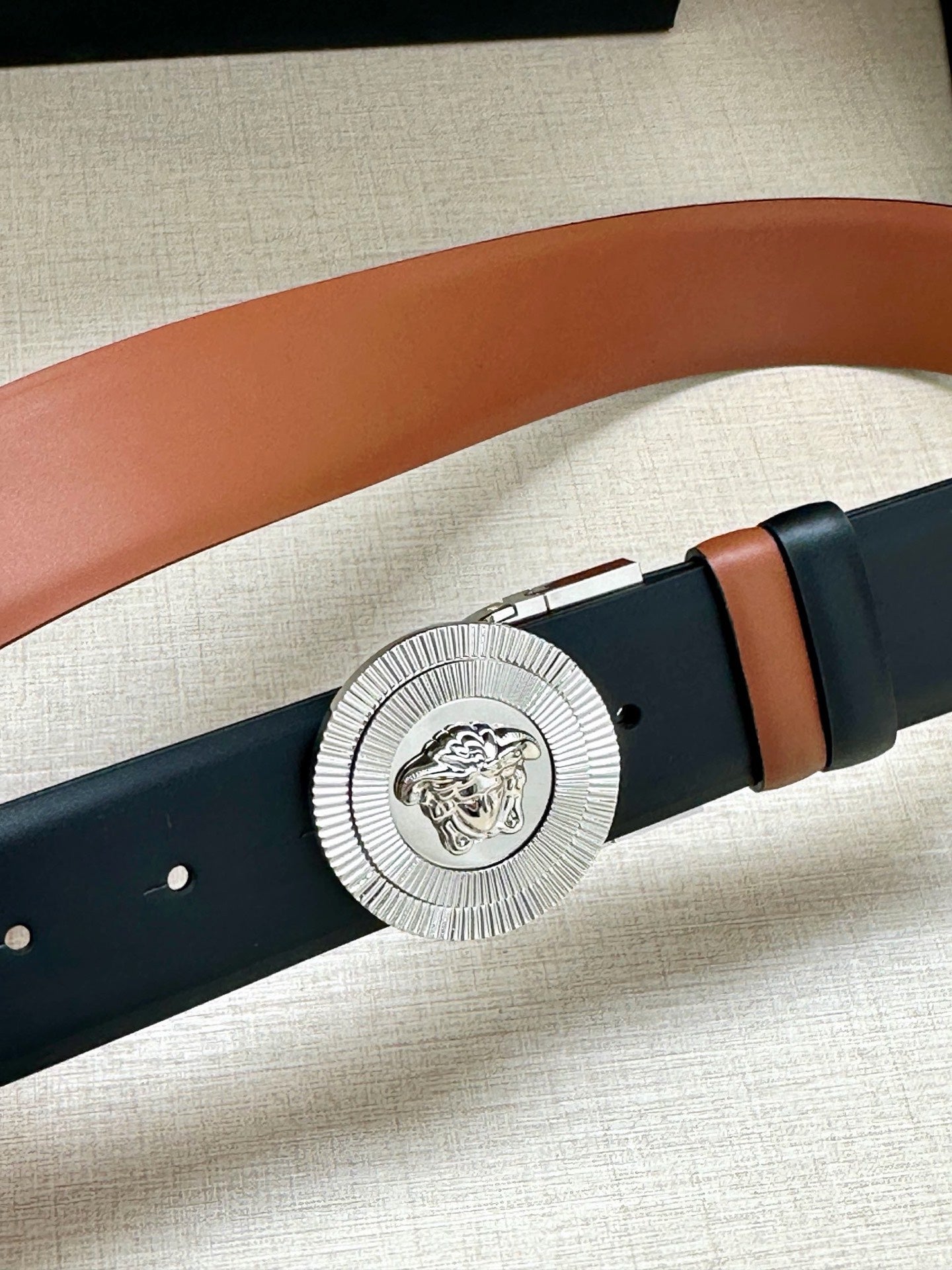 Dark navy belt with round silver Medusa buckle and tan edge paneling