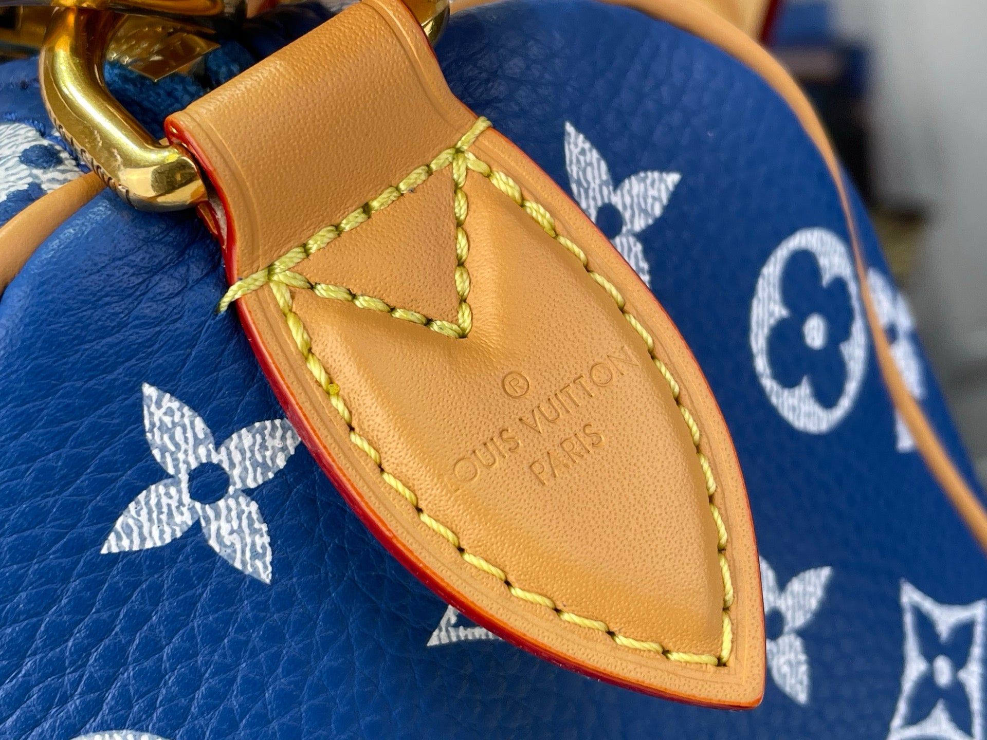 Louis Vuitton blue monogram bag close-up of tan leather tab with logo engraving