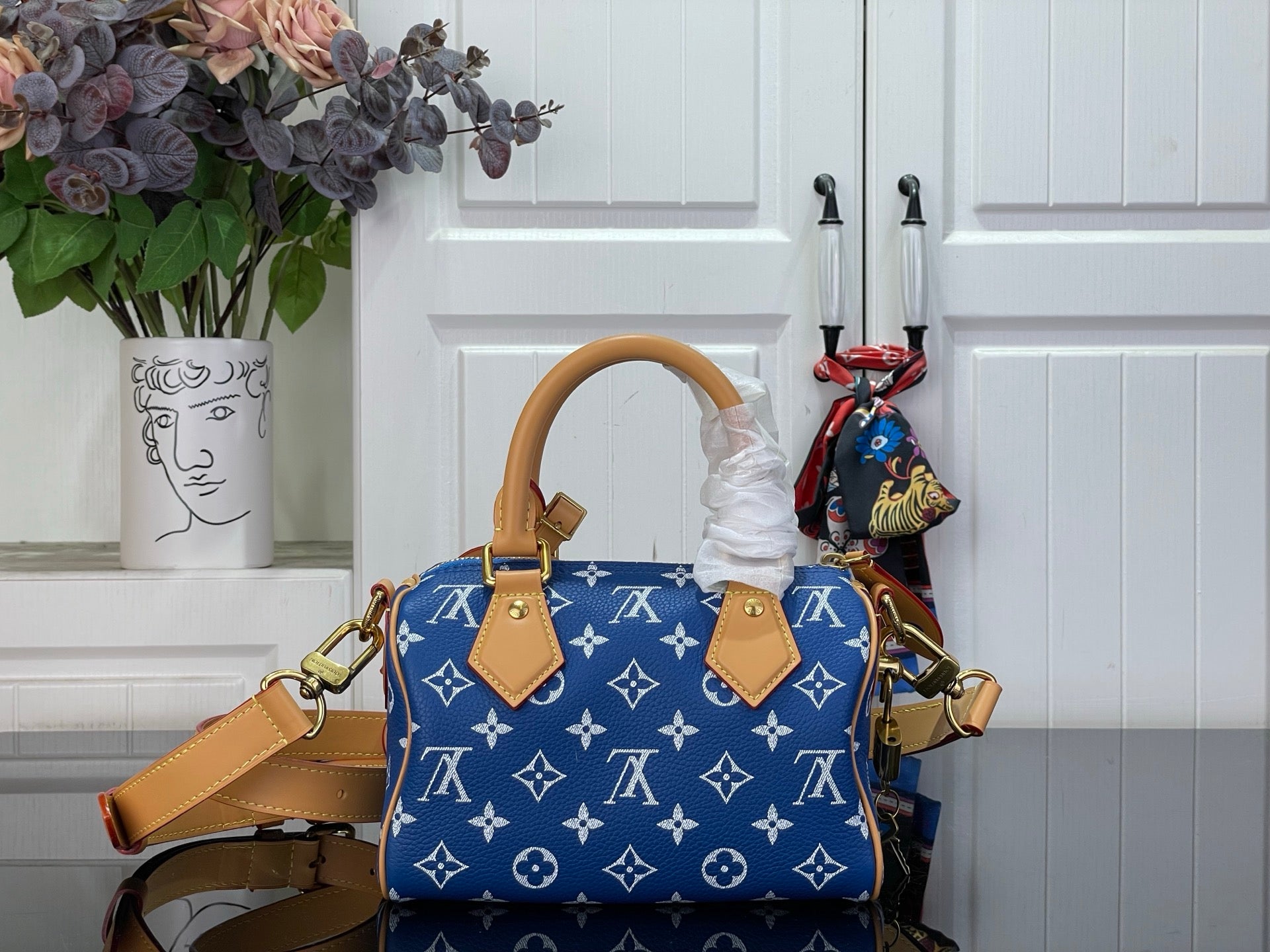 Louis Vuitton blue monogram handbag with tan strap and top handles, angled view