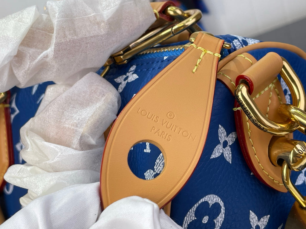 Louis Vuitton blue monogram bag with tan oval logo tag attached to the strap