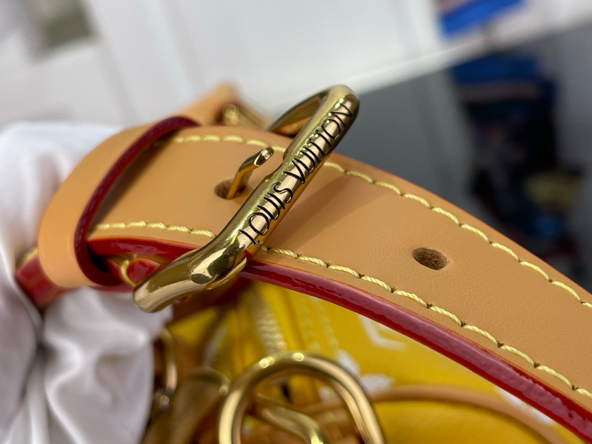 Louis Vuitton bag clasp and tan strap with stitched edge and metal hardware.