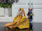 Designer handbag with yellow monogram print, tan top handle, and long shoulder strap