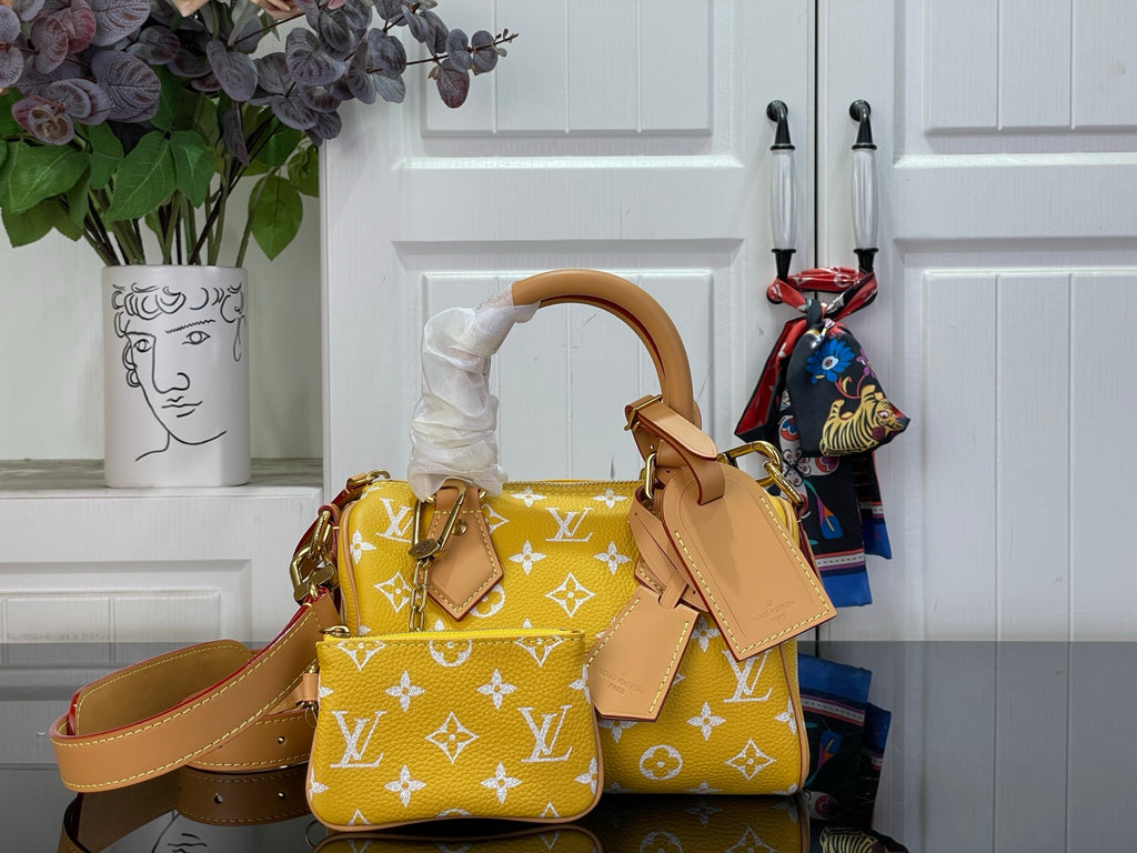 Designer handbag with yellow monogram pattern, tan leather handles, and top flap