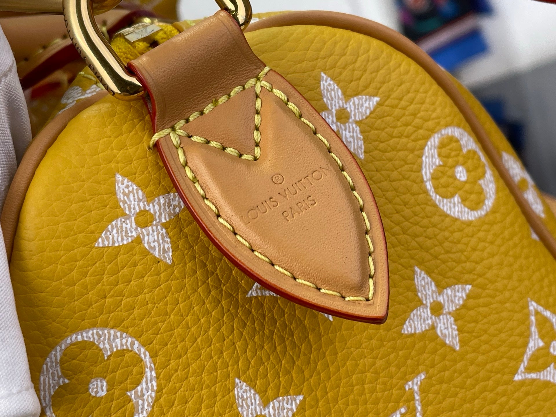 Designer handbag close-up: tan label with stitched edge on yellow monogram body