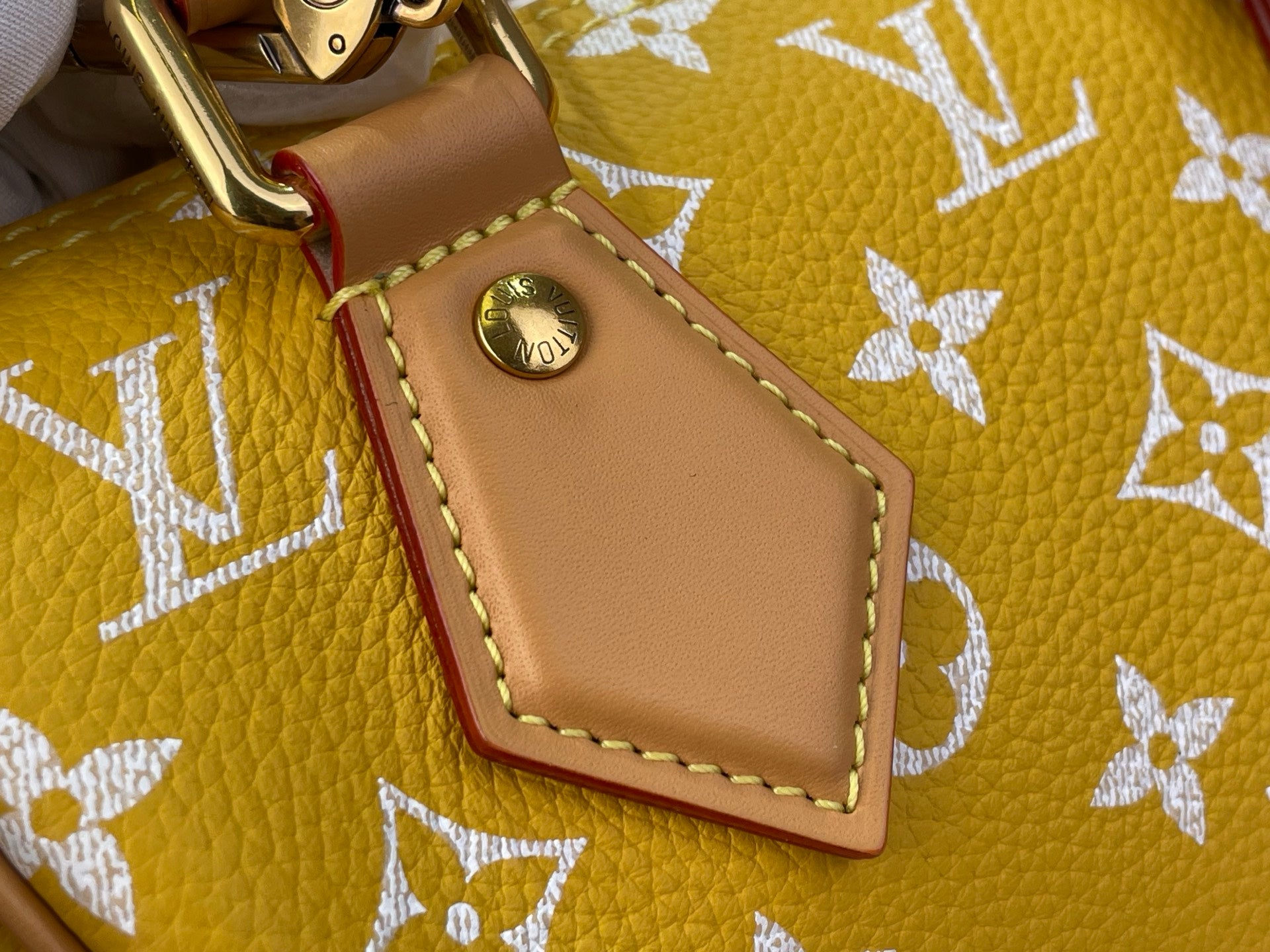 Designer handbag close-up of tan leather trim and round metal hardware on yellow monogram