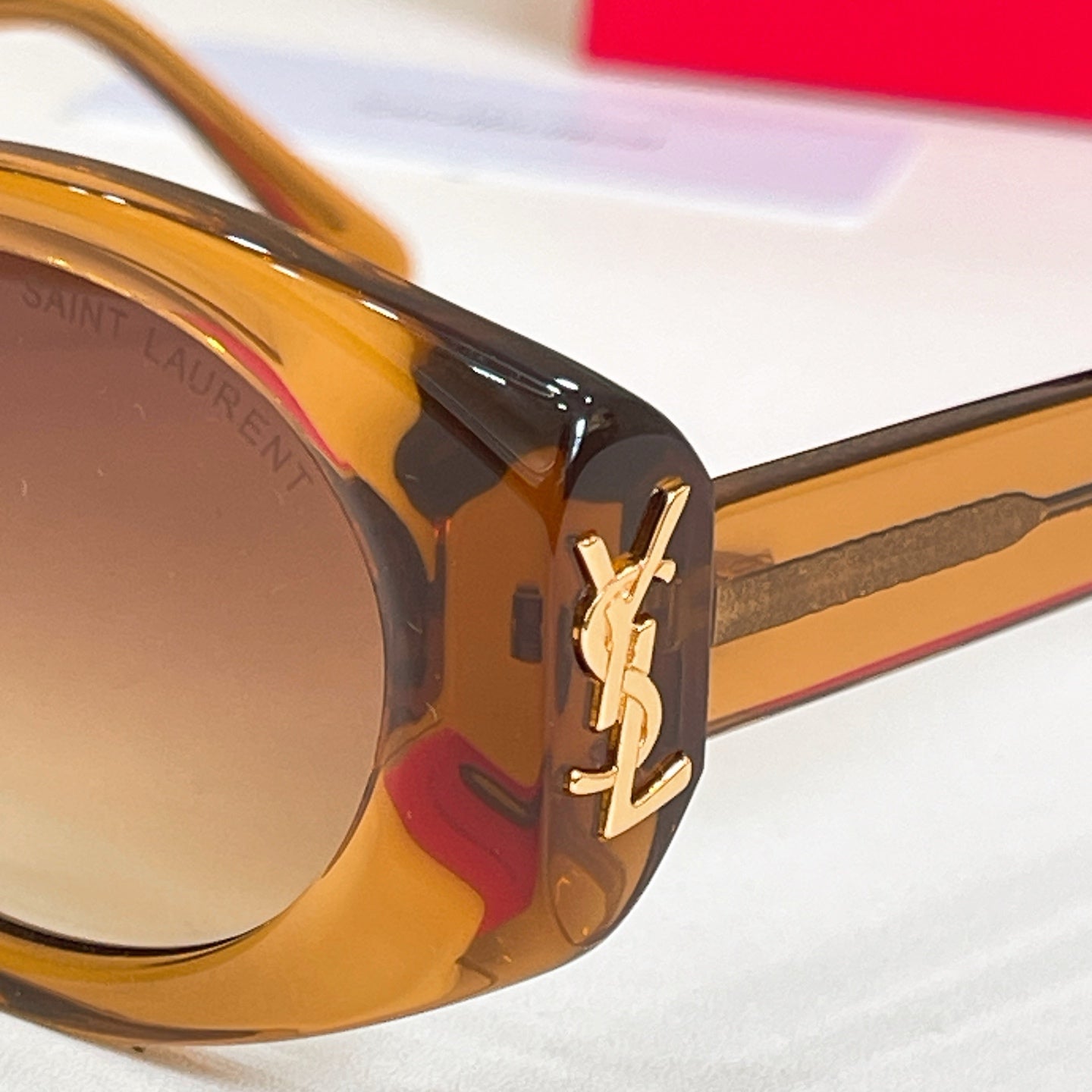 Close-up of amber acetate eyeglass frame with gold YSL logo on temple