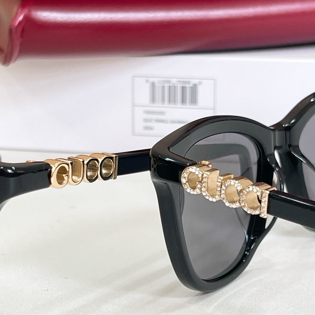 Gucci sunglasses, close-up black frame with gold-tone GG bar detail and gray lenses