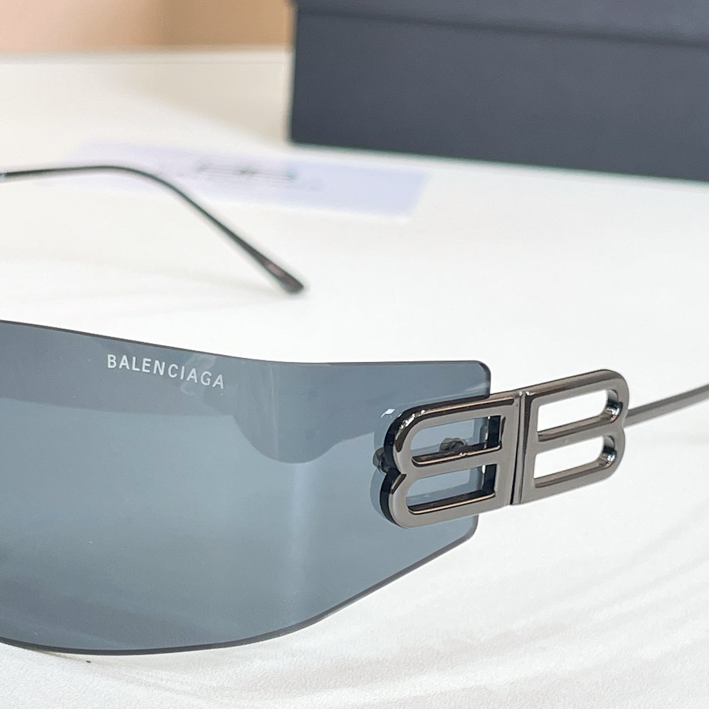 Sunglasses temple close-up with gold B logo and dark tinted lens, metal frame
