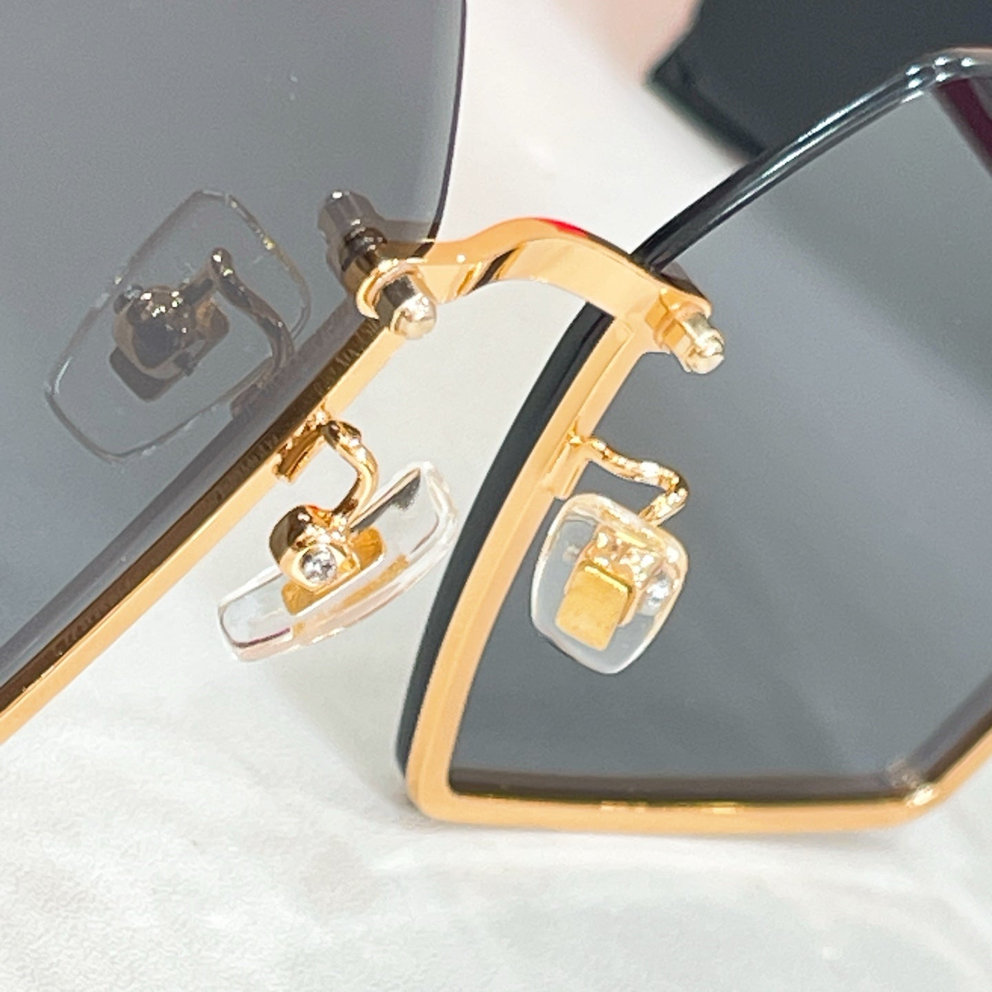 Glasses front corner with clear lens, gold logo embellishment, and dark frame