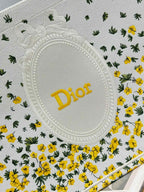 Dior oval logo patch on white tote bag fabric with yellow floral and cactus print.