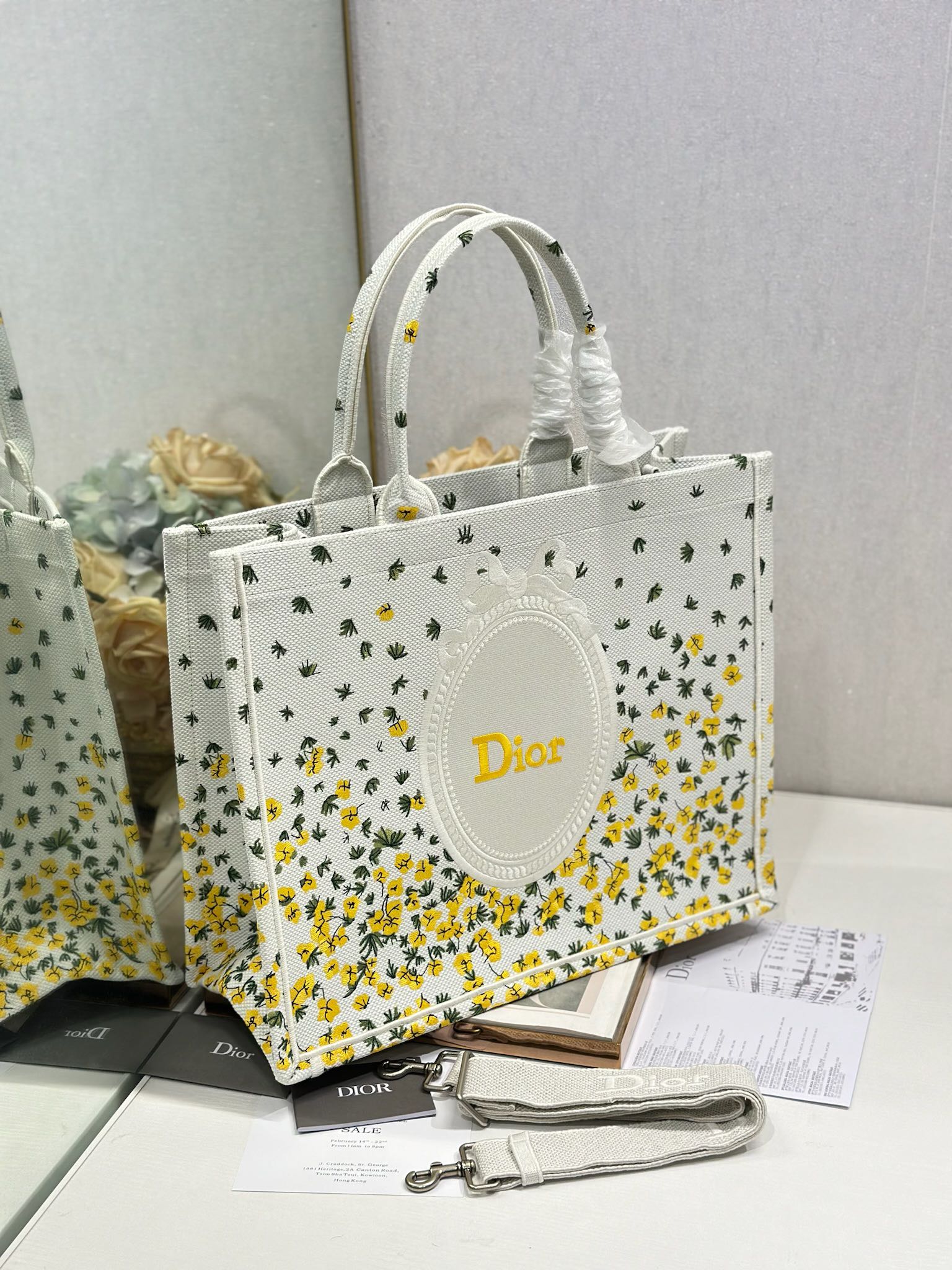 Dior tote bag with white fabric and yellow floral cactus print, oval Dior logo and handles.