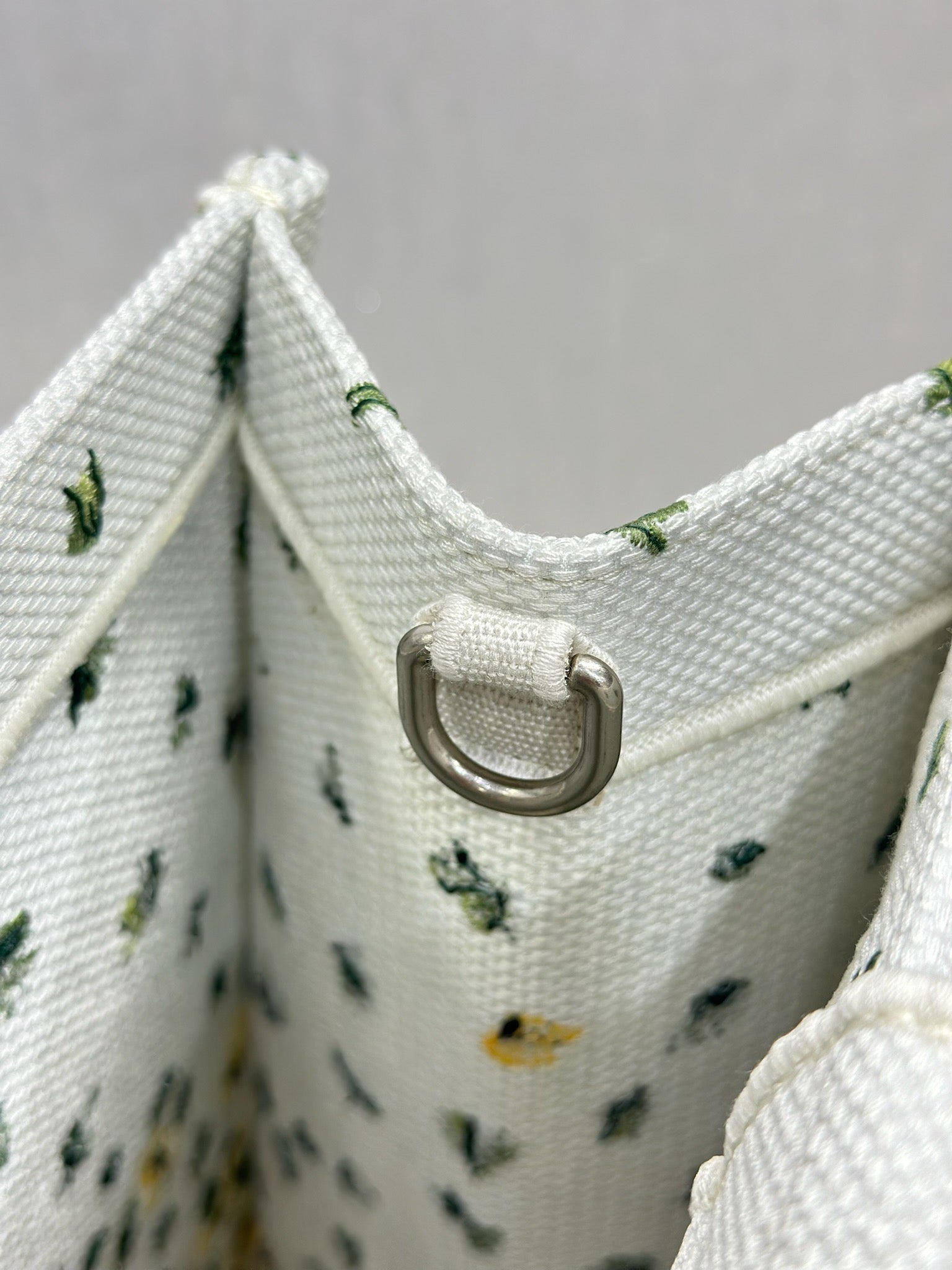 Dior tote bag top edge with metal snap ring on white fabric, yellow floral and cactus print.