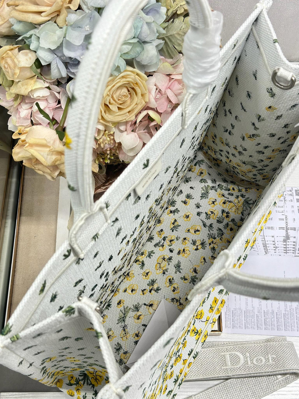 Dior tote bag angled with white fabric, yellow floral and cactus print, visible interior.