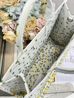 Dior tote bag angled with white fabric, yellow floral and cactus print, visible interior.