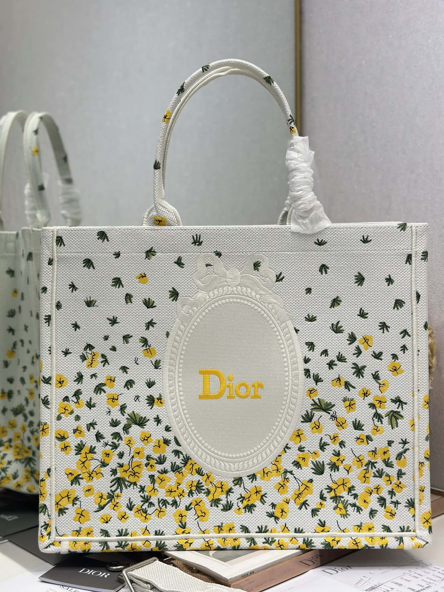 Dior tote bag front view in white fabric with yellow floral and cactus print, oval Dior patch.