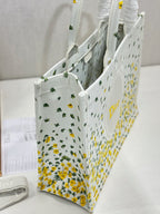 Dior tote bag shown from the side, white fabric with yellow floral and cactus pattern.