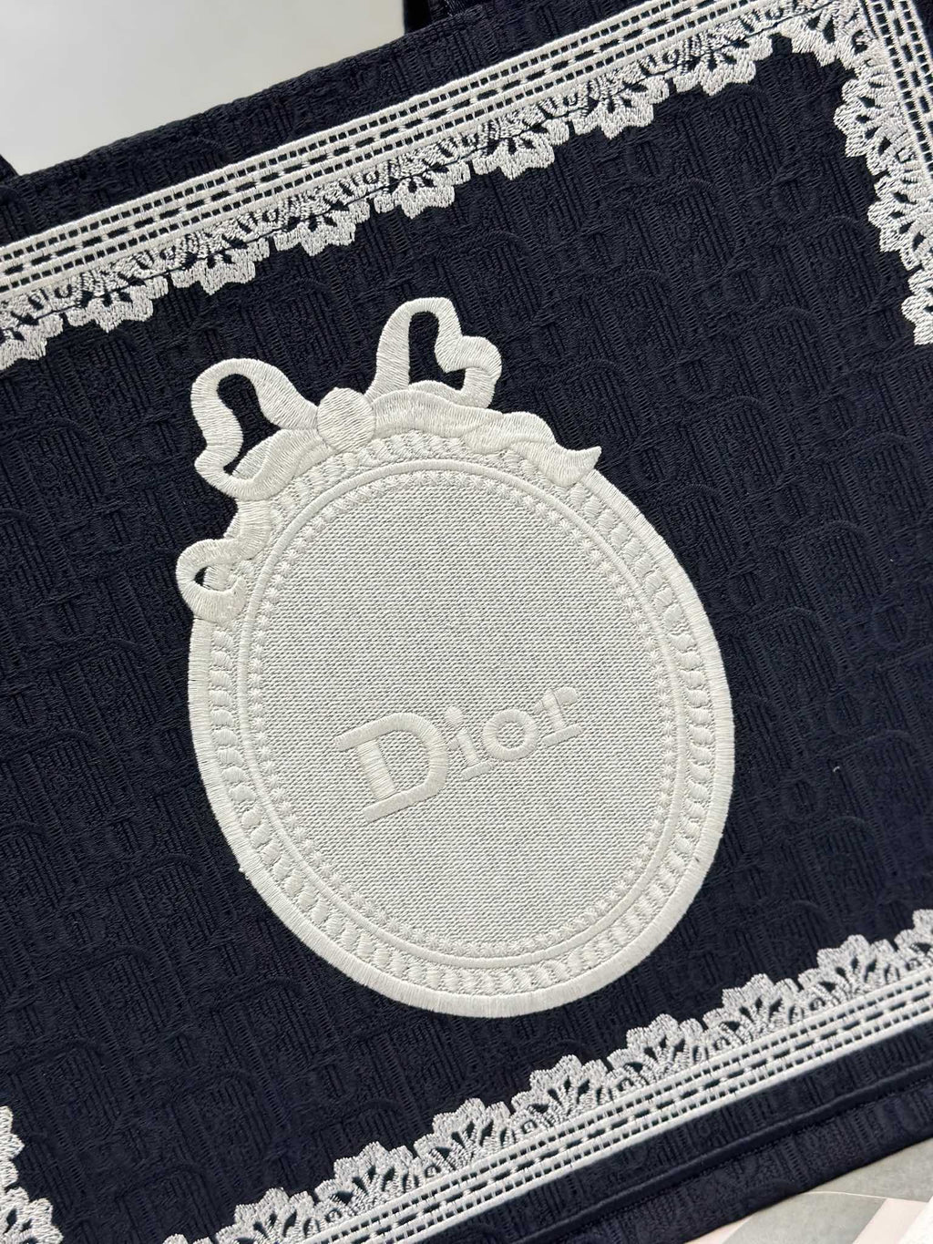 Close-up of navy Dior tote bag front with embossed white medallion logo and trim