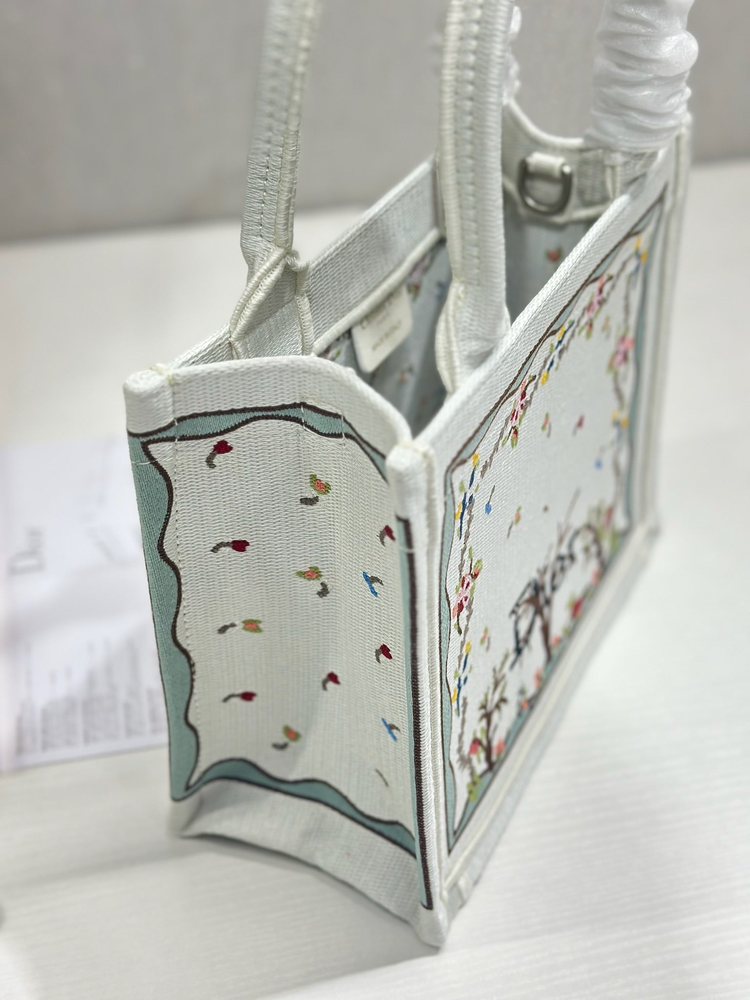 Dior tote bag side view with embroidered panel and light gray interior fabric