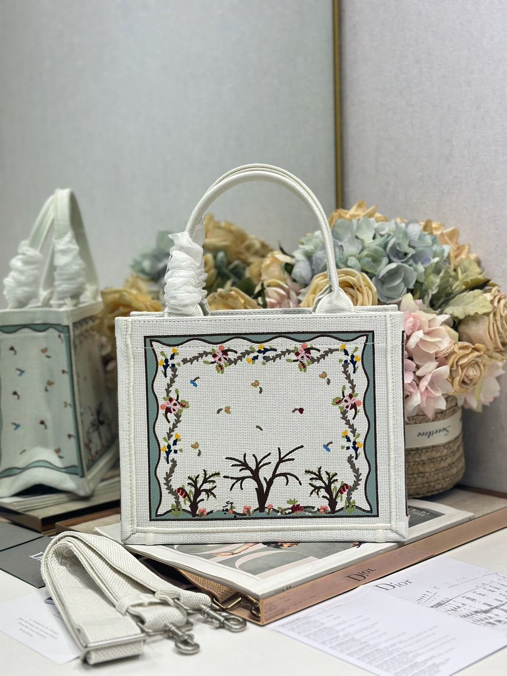Dior tote bag with light gray canvas, embroidered nature scene panel, and rounded handles